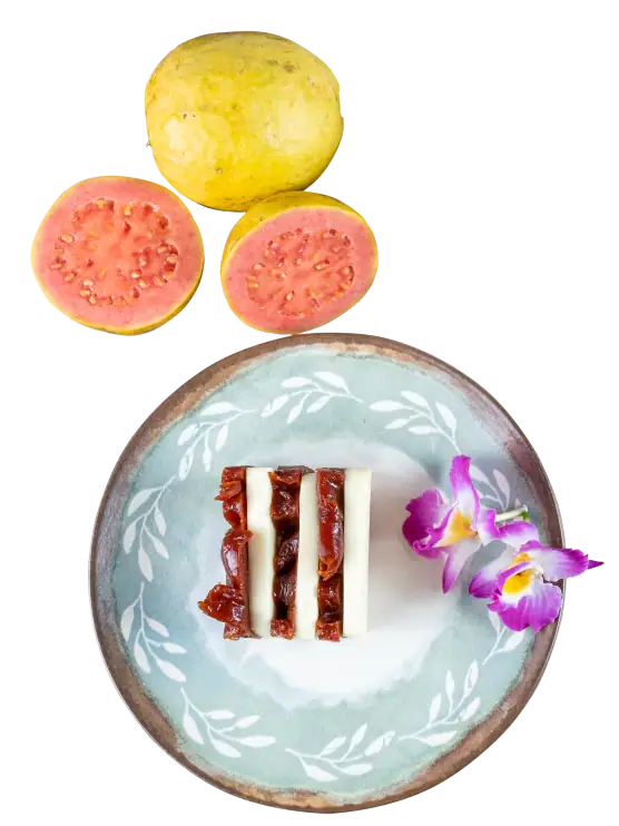 Fresh yellow and pink guava fruits with a slice of layered cake decorated with edible flowers on a light blue plate.