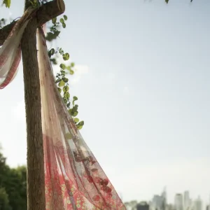 A piece of sheer fabric with floral patterns draped over a wooden pole outdoors, with a city skyline in the background under a partly cloudy sky.