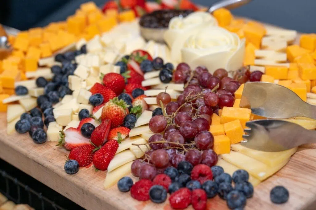 Assorted cheese platter with strawberries, blueberries, red grapes, and cheese cubes, served on a wooden board at The Enchanted Event C. Perfect for guests to enjoy a variety of flavors and textures.